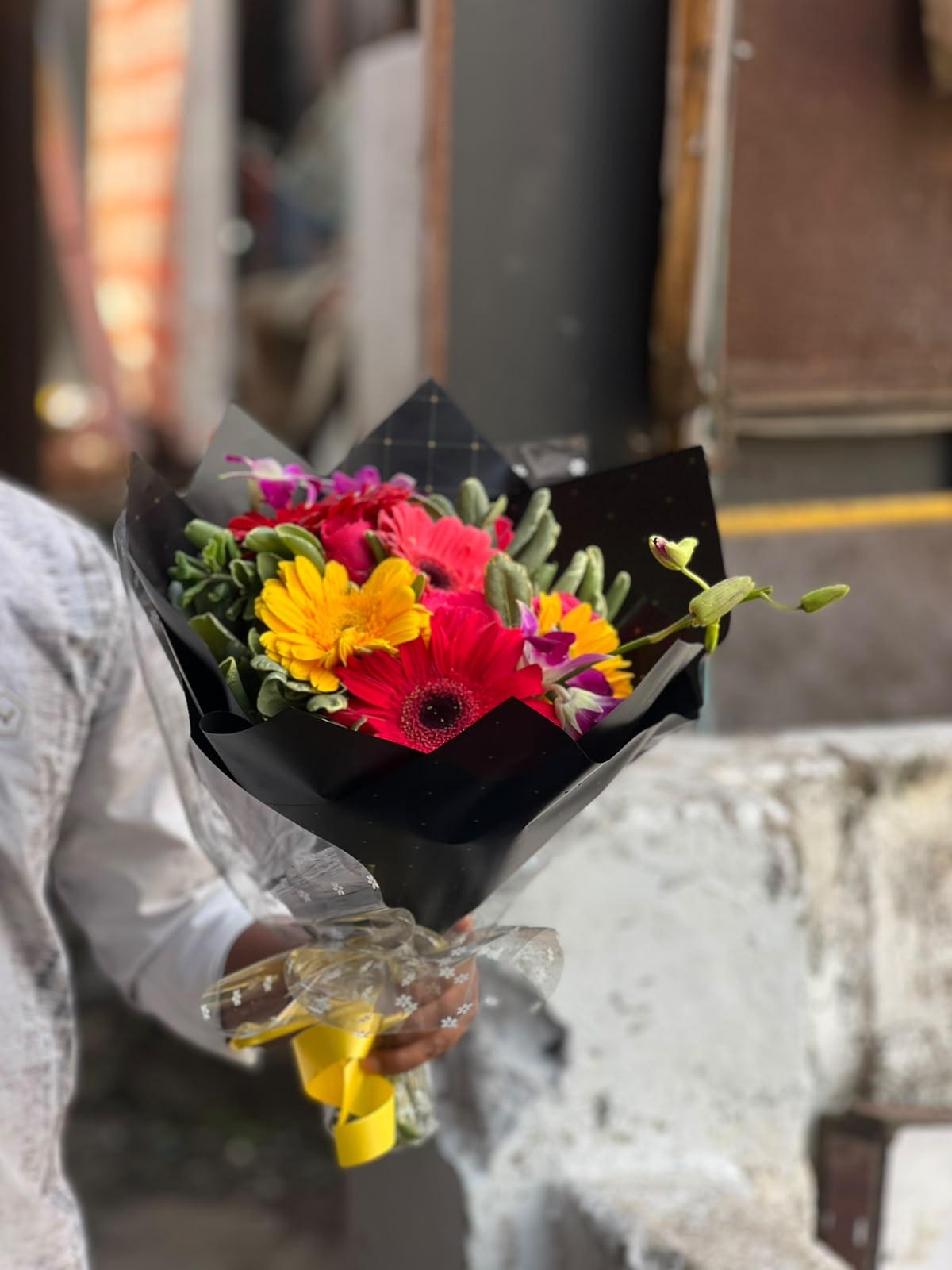 Vibrant yellow, coral and red gerberas with purple orchids wrapped in noir paper in Ooty