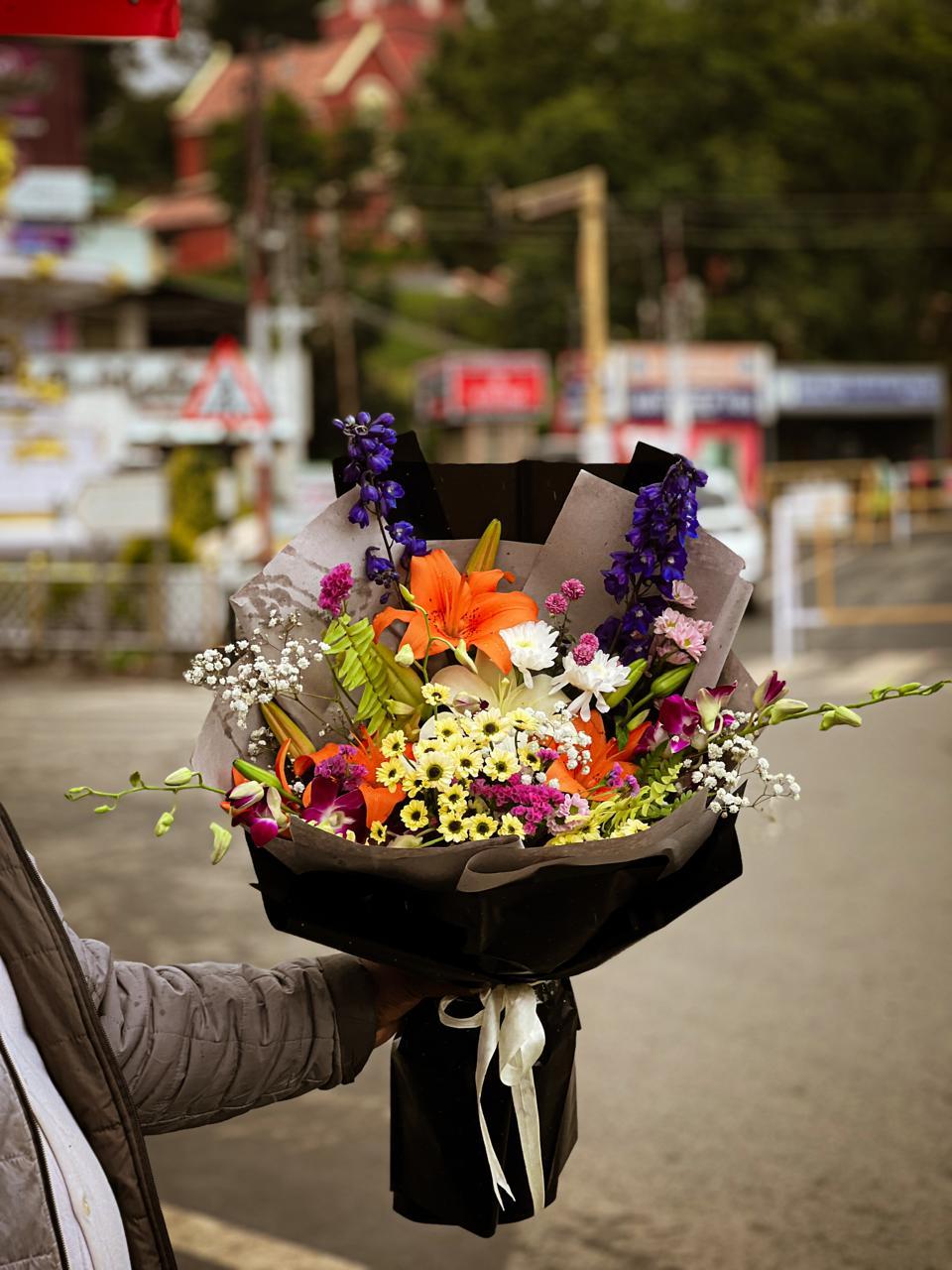 Majestic wild flower bouquet with blue delphiniums, orange lilies, orchids and chamomile in Ooty